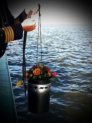 Ansicht einer Seebestattung - Urne wird von einem Schiff aus zu Wasser gelassen